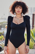 Load image into Gallery viewer, You&#39;re sure to turn a head and drop a jaw with this puff-sleeved bodysuit. It&#39;s perfect for adding to any outfit of the day. Featuring a black stretchy ribbed material with puff long-sleeves, Sweetheart neckline, padded cups, and attached thong bottoms with snap closures. Team it with some light wash jeans, cute high heels, layered jewelry, and a clutch purse for a fun and flirty look. 
